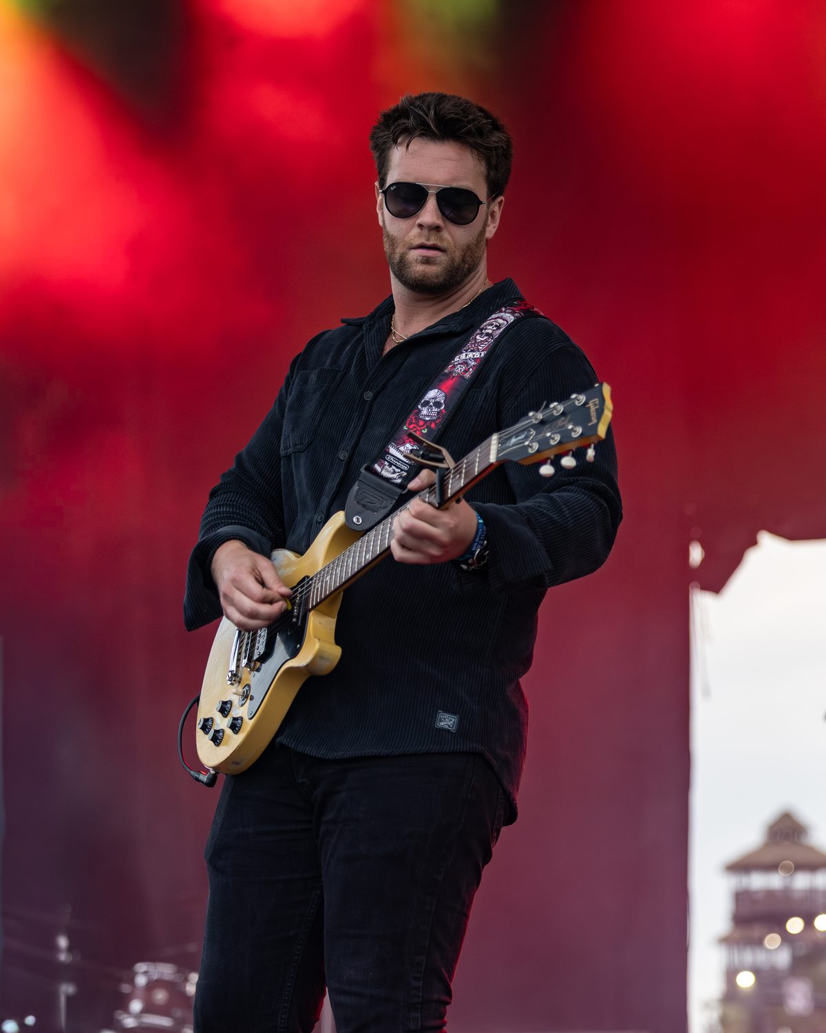 Brian Lawless playing a gold Gibson Les Paul under red stage lights at a summer festival